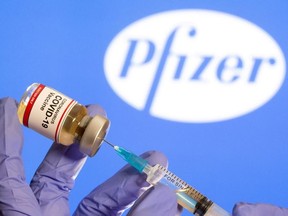 A woman holds a small bottle labelled with a "Coronavirus COVID-19 Vaccine" sticker and a medical syringe in front of displayed Pfizer logo in this illustration taken Oct. 30, 2020.