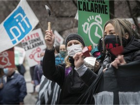 A protester wearing a mask gestures. There are many protesters with signs behind them.