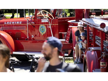 A woman and child try to find some shade from an antique ladder truck on display as part of the Canadian Firefit Championships and picnic day, in Montreal, on Saturday, July 2, 2022.