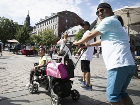 Tourist Larry Rosario pushes his seven-year-old daughter Angelie and Alexandra Javier during a walk in Place Jacques-Cartier on Monday, July 11, 2022.