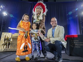 Denis Gros-Louis, right, director general of the First Nations Education Council, presents the wampum and a talking stick to Régis Penosway, chief of the Kitcisakik First Nation, and his daughters Deanna, left, and Aimé during a ceremony marking an agreement between the federal government and 22 First Nations advancing their control over education, in Kahnawake, Thursday July 14, 2022.