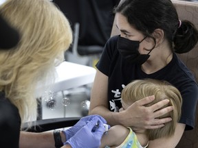 Nadia Mimouni holds her 2 1/2-year-old son, Vincent Zimmerman Mimouni, as he is given a COVID-19  vaccination at Décarie Square in Montreal on Monday, July 25, 2022.