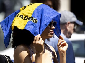A woman covers her head from the sun with the flag of Barbados during the Carifiesta Parade in Montreal, on Saturday, July 2, 2022.