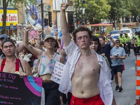 People silently raise their arms while walking on St-Laurent Blvd. in Montreal Sunday, Aug. 7, 2022. This was during a protest march that was made after the Pride Parade was cancelled.