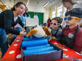 First grade students Schlok Sharma, right, and Sebastian Rodriguez Chaparro wear dark glasses to watch as McGill first-year medical student Jenna Gregory guides their stuffed animals through a mock x-ray machine.