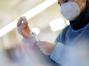 a nurse is preparing a dose of vaccine. she is wearing a mask.