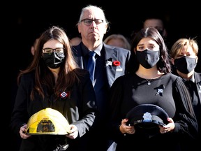 The daughters of firefighter Pierre Lacroix, Stephanie and Annick, carry his helmet and his dress cap as they leave his funeral at Notre-Dame Basilica in October 2021. Yves Lacroix, Pierre’s brother, follows behind them.