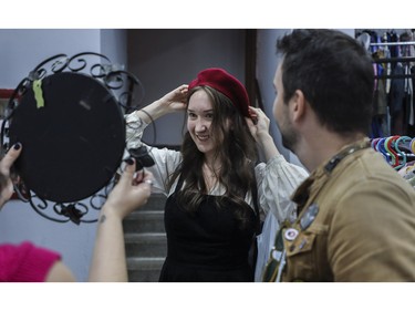 Alana Shahbazian looks at herself in a mirror as she tries on a beret at a vintage bazaar at Saint-Jean-Berchmans Church in Montreal on Sunday, Oct. 23, 2022. Watching is her friend Bart Aupetit.