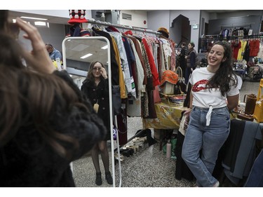 Patricia Charron of the online boutique The Kashan Closet looks on as Alana Shahbazian tries on a coat and sunglasses at a vintage bazaar at Saint-Jean-Berchmans Church in Montreal on Sunday, Oct. 23, 2022.