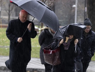 A pedestrian wraps her broken umbrella around her head as wind and rain begin to build in Montreal Nov. 30, 2022.