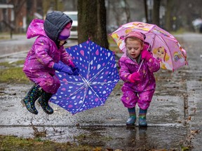 Not-quite-cookie-cutter twins Blake, left, and Avery Preston jump in a puddle while waiting with their mother Jessica Kirzner to pick up their big brother after school in Pointe-St-Charles Nov. 30, 2022.