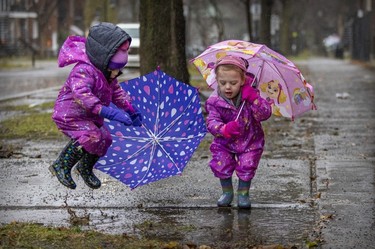 Two-year-old twin sisters Blake, left, and Avery Preston jump in a puddle while waiting with their mother Jessica Kirzner to pick up their big brother after school in Pointe-Saint-Charles on Nov. 30, 2022.
