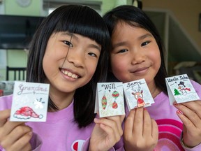 Nine-year-old friends Sofia Zhang, left, and Sophie Ha,  display some of the individualized Christmas-theme name tags in Dollard-des-Ormeaux that they decided to draw to sell to the community to save up money to purchase items on their Christmas wish lists.