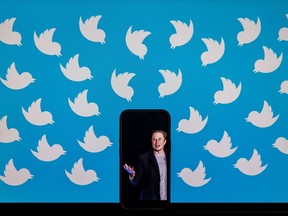 A cellphone displaying a photo of Elon Musk placed on a computer monitor filled with Twitter logos.