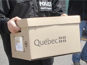 A Sûreté du Québec officer carries documents away after a search.