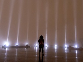 A woman braves the rain to take a moment in silence as the sky is lit with 14 beams of white light during ceremonies to mark the anniversary of the massacre at Ecole Polytechnique in Montreal, on Tuesday, Dec. 6, 2022.