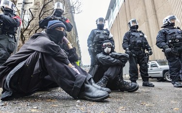 Anti-capitalist demonstrators sit down in front of a row of riot police during protest against the COP15 conference in Montreal on Dec. 7, 2022