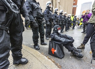 Anti-capitalist demonstrators sit down in front of a row of riot police during protest against the COP15 conference in Montreal on Dec. 7, 2022