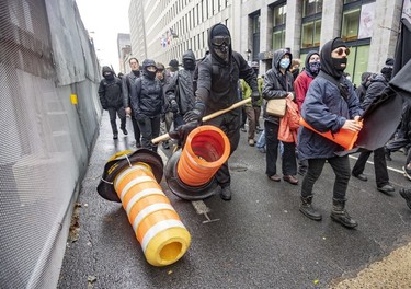 An anti-capitalist demonstrator knocks down orange cones outside the Palais des congrès in Montreal on Dec. 7, 2022