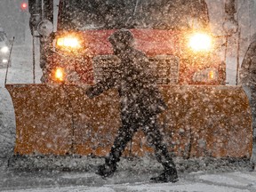 A pedestrian can hardly be seen amid the falling snow as he passes in front of a snowplow along René-Lévesque Blvd. on Friday.