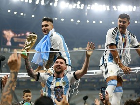 Argentina's Lionel Messi celebrates winning the World Cup with the trophy as Argentina's Lautaro Martinez and Paulo Dybala sit on a goal frame at Lusail Stadium in Lusail, Qatar, on Sunday, Dec. 18, 2022.