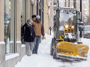 Pedestrians press themselves against a wall to let the sidewalk plow go by on Peel St. Jan. 26, 2023.