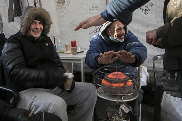 Ewans Stanich, left, and Keith Upshaw sit around a heater on a cold day at Resilience Montreal, December 12, 2022.