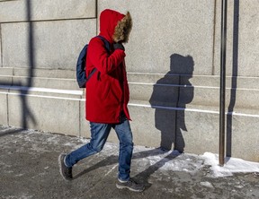 A pedestrian holds his hood closed while walking on René-Levésque Blvd. on a bitterly cold and windy day in Montreal on Friday, Feb. 3, 2023.