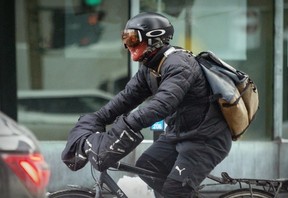 A bicycle messenger covers up his face against the wind on a bitterly cold and windy day in Montreal on Friday, Feb. 3, 2023.