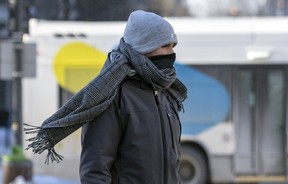 A pedestrian uses a neck warmer and a scarf to battle the elements on a bitterly cold and windy day in Montreal on Friday, Feb. 3, 2023.