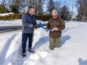 Henry Ornawka (right) stands in ditch recently dug by the town of Baie-D'Urfé while speaking with neighbour Jacques Poulin, holding a broken tow strap from an Amazon delivery truck that tipped over into the ditch recently on Lakeview St. Poulin has counted over a dozen vehicles that have ended up in the ditch in the last six weeks.