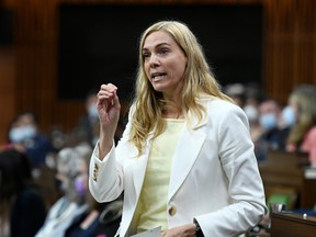 A woman in a white suit with blonde hair is standing and gesturing in the Canadian house of commons.
