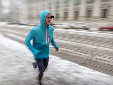 A runner keeps his hood on against blowing snow on a cold, windy day in Montreal Thursday Feb. 23, 2023.