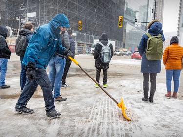 Scott Lowson keeps the corner of Guy St. and Ste-Catherine St. clear of snow on a cold, windy day in Montreal Thursday Feb. 23, 2023.