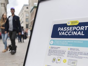 People walk by a sign outside a restaurant advising customers of the Quebec government's newly implemented COVID-19 vaccine passport in Montreal, Monday, Sept. 6, 2021. Quebec anti-corruption police say a former employee of a Montreal health authority is facing criminal charges after she allegedly made fake proof of COVID-19 vaccinations.