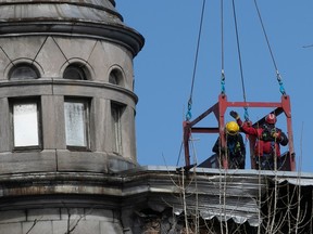 Montreal firefighter and a member of the demolition crew are hoisted on a work platform at the scene of the aftermath of fire in Old Montreal on March 22, 2023.