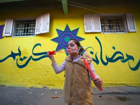 A child blows soap bubbles as she stands in front of a wall, painted in vivid colours and Arabic calligraphy that reads "Ramadan Karim" as part of an initiative by a Palestinian artist, in the Zeitun district of Gaza City.