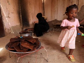 A child plays as a Sudanese woman prepares Helo Murr, a Ramadan drink made with dried corn and spices which is then dipped in water, in a village south of Khartoum ahead of the Muslim holy fasting month of Ramadan.