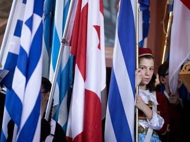 A young girl peeks out from behind a row of flags as she takes part in a special service at the Greek Orthodox Church Evangelismos Tis Theotokou as part of the Greek Independence Day celebrations in Montreal on Sunday, March 26, 2023.
