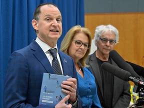 Quebec Finance Minister Eric Girard holds a copy of the provincial budget speech March 20, 2023. With him are Quebec Minister of Families Suzanne Roy, centre, and Dr. Gilles Julien.