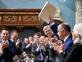 Quebec Health Minister Christian Dubé, right, waves a copy of legislation on health he just tabled, Wednesday, March 29, 2023 at the legislature in Quebec City.
