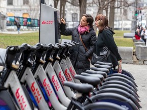Tourists Emma Hueso, left, and Barbara Bauer check out the prices for renting a Bixi in Old Montreal as the bike-sharing service launches its season on Wednesday April 12, 2023.