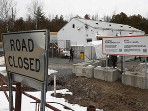 There are white buildings and a border crossing sign in the background and a "road closed" sign in the foreground.