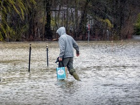 A man carries groceries to his home on a flooded street as the Ottawa River spills its banks in Rigaud, west of Montreal on Monday, May 1, 2023.