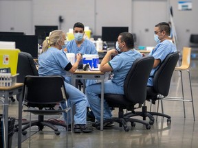 Four health care nurses in blue scrubs at talk around a table at a vaccination clinic