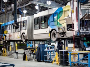 An articulated STM bus is hoisted on a lift in a garage.