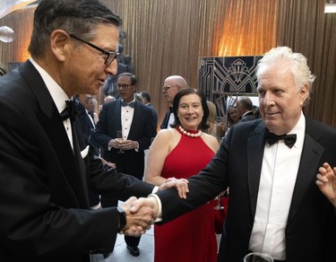 Two men in tuxedos shake hands at a black-tie event