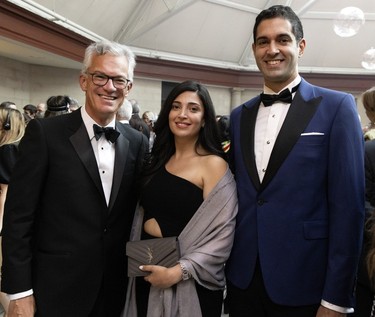 A woman flanked by two men in tuxedos at a party