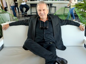 Michel Cote in a black suit lounging on a white sofa