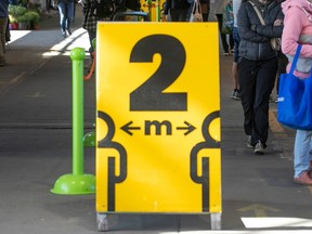 A yellow sign at a public market with bold black writing to keep 2 metres apart